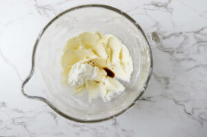 Adding sour cream and vanilla extract to a mixing bowl with frosting.
