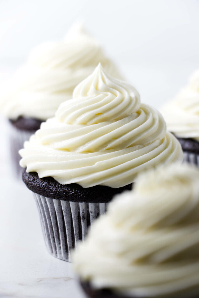 Chocolate cupcake with white frosting in focus, others blurred behind.