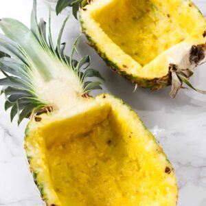 Empty pineapple shells with green tops on white marble surface.