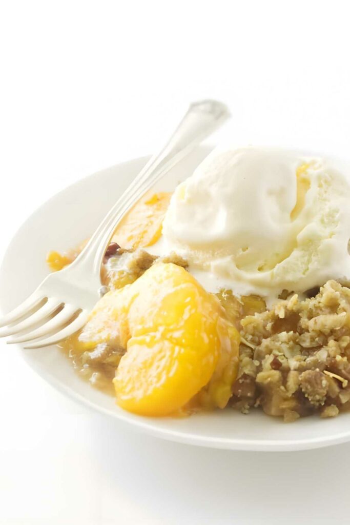 Peach crisp and vanilla ice cream on a white plate with a fork.