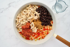 Adding shredded chicken, beans, salsa and seasoning to a skillet.