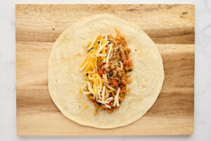 Adding chicken filling to a flour tortilla for a burrito.