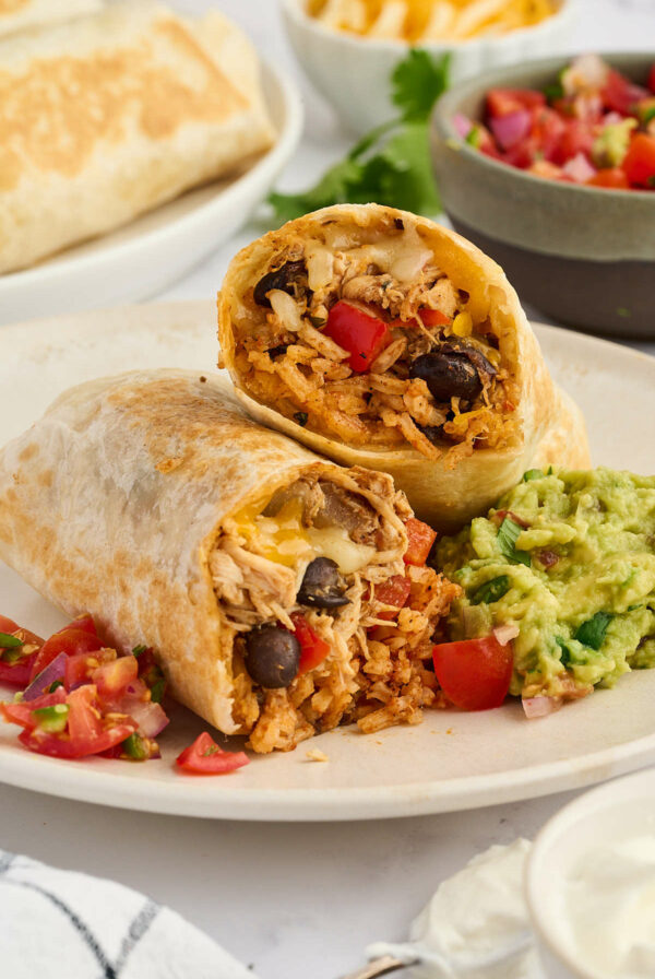 Halved burrito with rice, beans, chicken; served with guacamole and salsa.