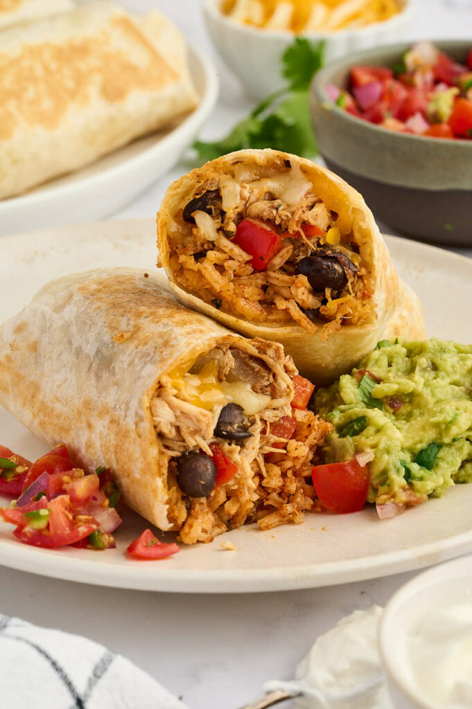 Halved burrito with rice, beans, chicken; served with guacamole and salsa.