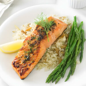 Baked salmon on rice with dill, lemon wedge, and steamed asparagus.