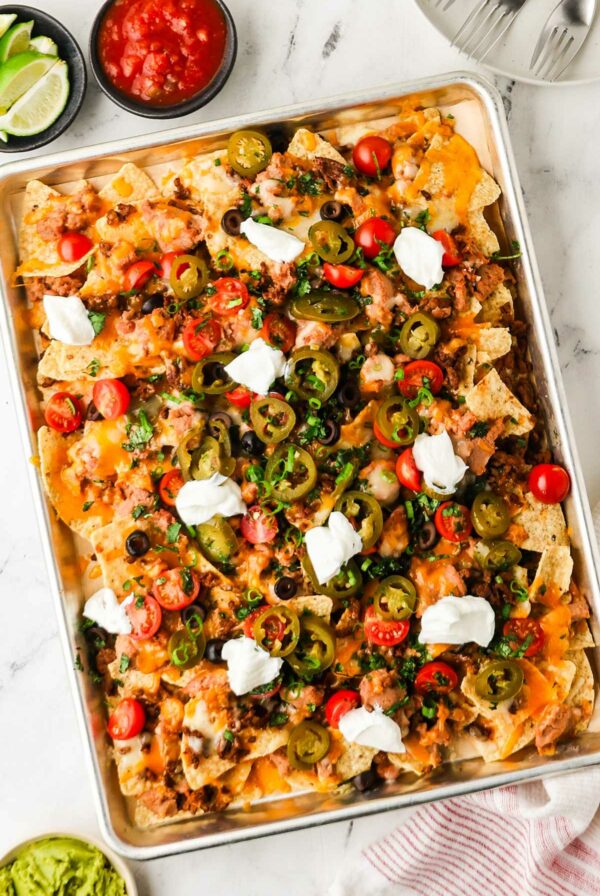Sheet pan nachos with cheese, meat, veggies, and sour cream; salsa on side.
