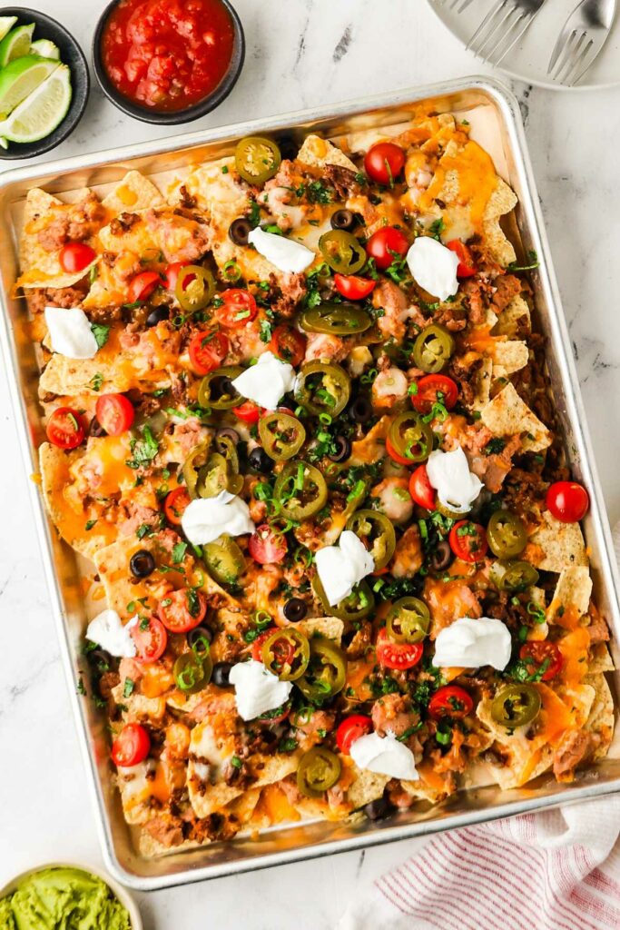 Sheet pan nachos with cheese, meat, veggies, and sour cream; salsa on side.