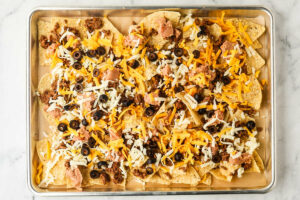 Adding a layer of toppings over some tortilla chips.