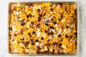 Layering cheese and olives over ground beef nachos.