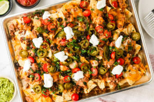 Ground beef nachos in a sheet pan topped with sour cream, tomatoes, and peppers.