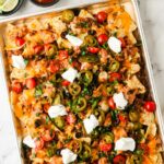 Loaded nachos on a sheet pan with cheese, ground beef, jalapeños, tomatoes, and sour cream.
