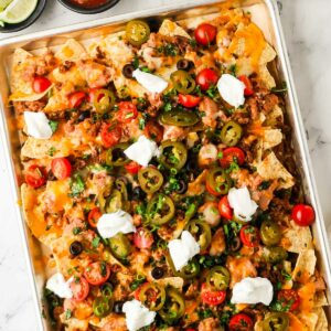 Loaded nachos on a sheet pan with cheese, ground beef, jalape&ntilde;os, tomatoes, and sour cream.