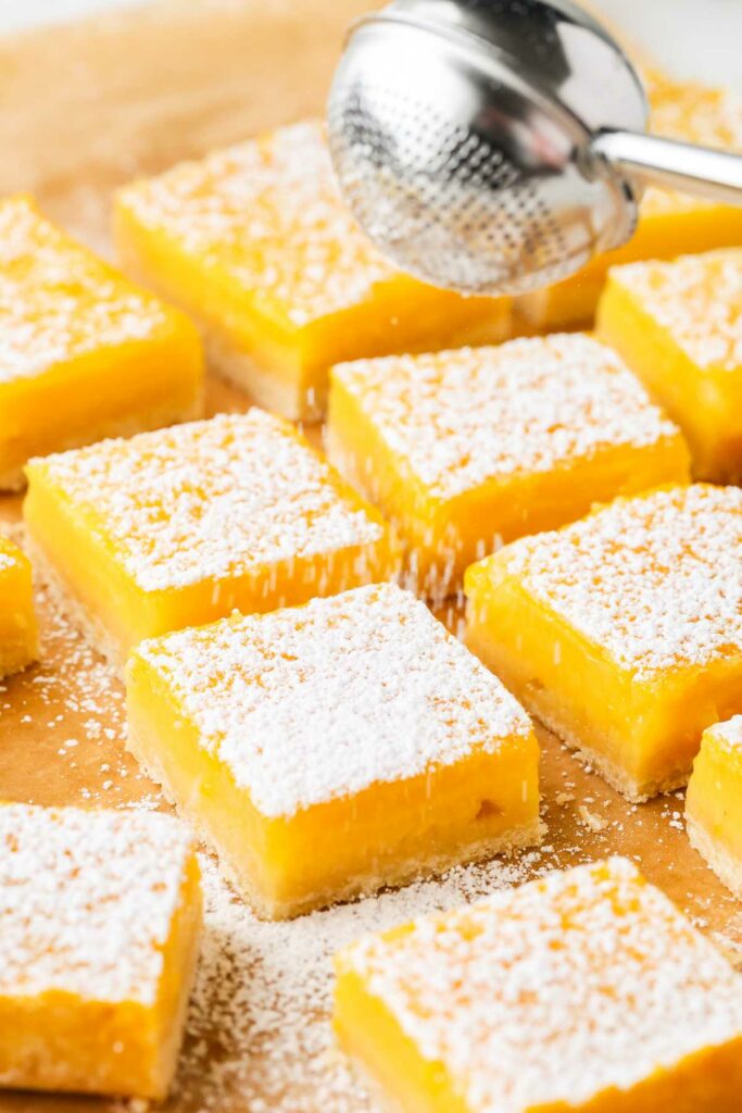 Dusting powdered sugar over lemon bar squares.