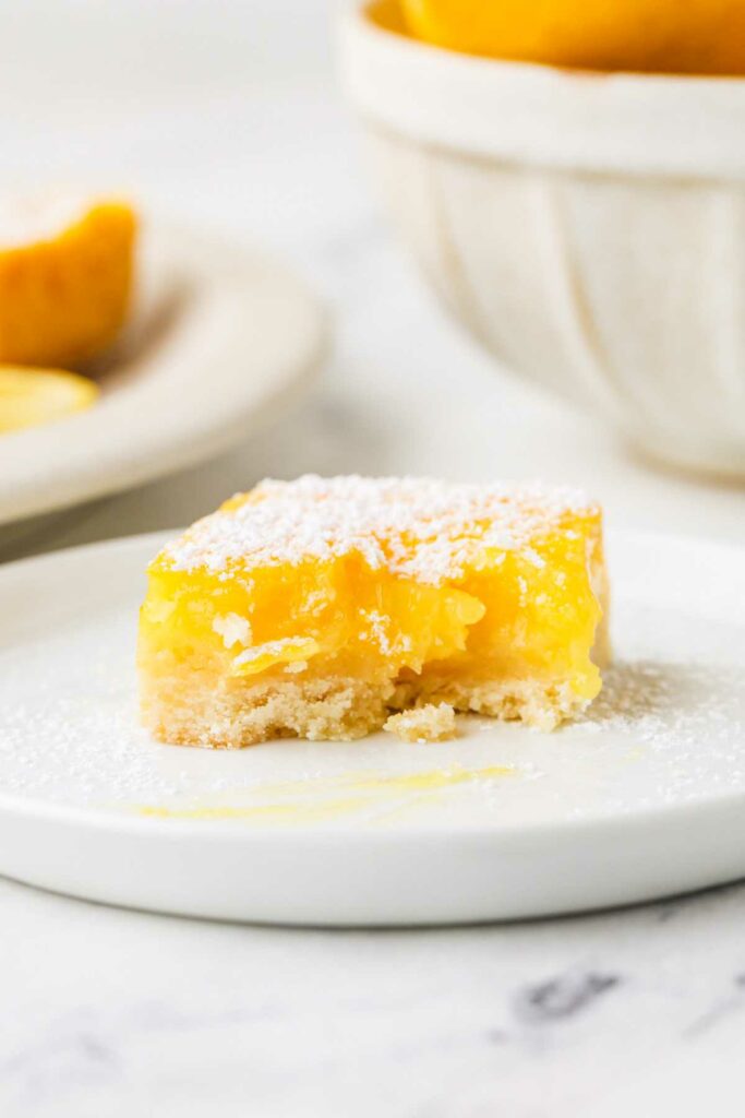 A partially eaten lemon bar on a white plate.