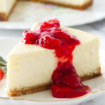 Strawberry sauce on a slice of cheesecake on a plate.