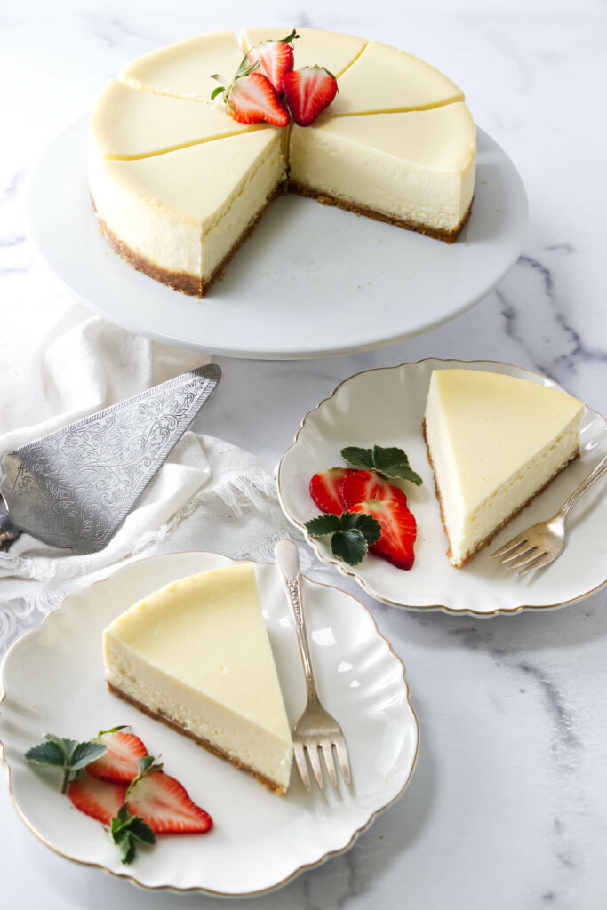 Cheesecake with strawberry garnish, sliced and served on plates with forks.