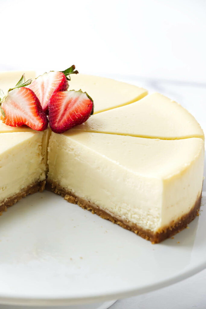 Sliced cheesecake with cookie crust and strawberries on a white plate.