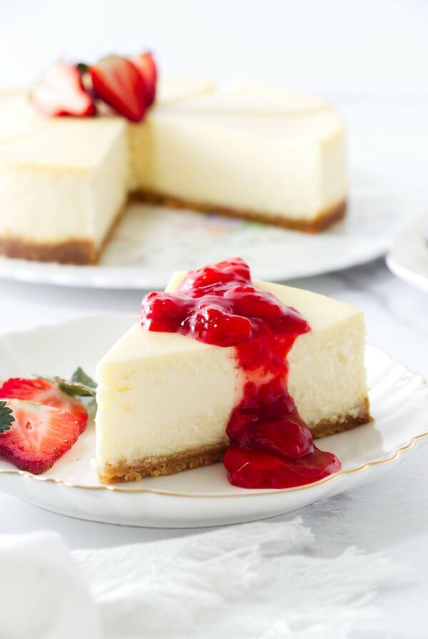 Cheesecake slice with strawberry sauce and fresh strawberries on a white plate.