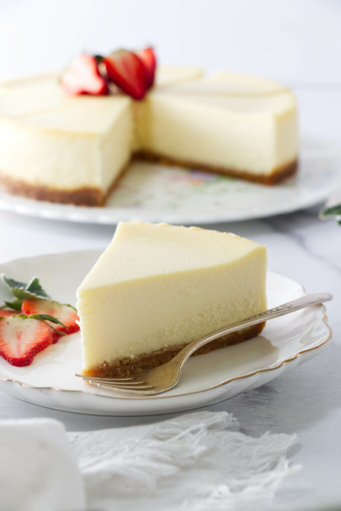 Slice of cheesecake baked with no water bath, whole cake in background.