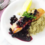 A fillet of salmon topped with blueberry sauce on a white plate.