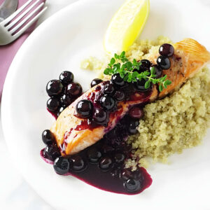 A fillet of salmon topped with blueberry sauce on a white plate.