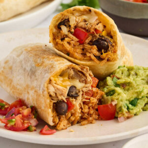 A chicken burrito cut in half and on a plate with guacamole.