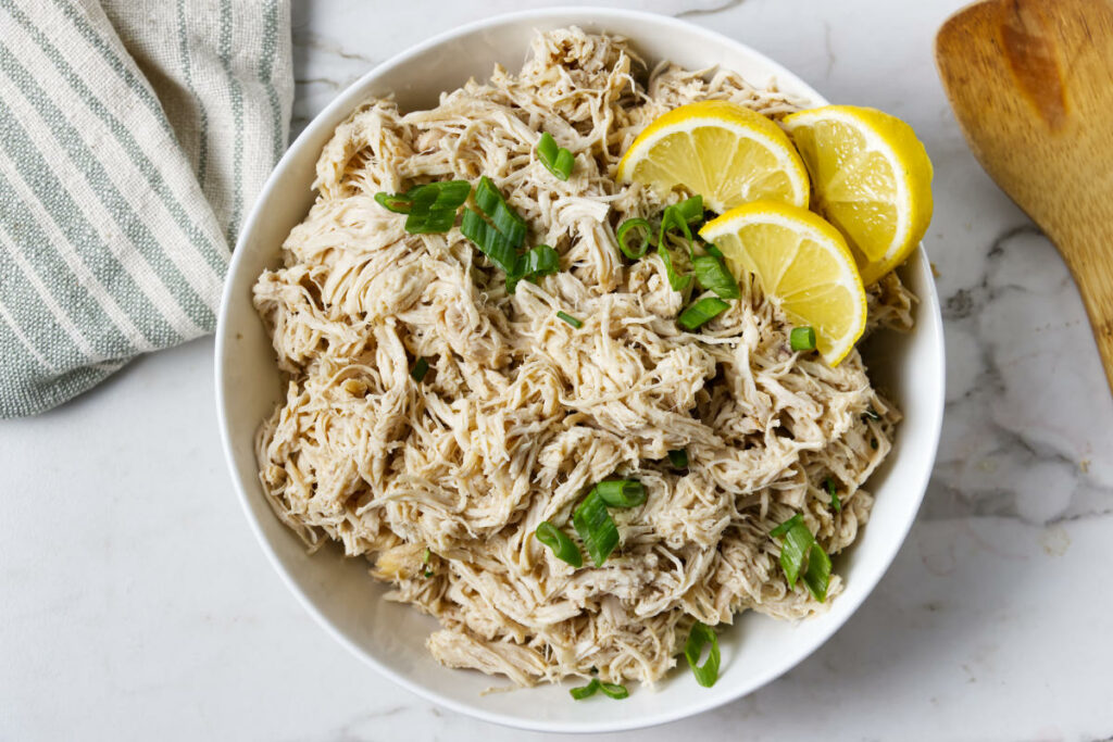 Shredded chicken in a white bowl topped with lemon slices.