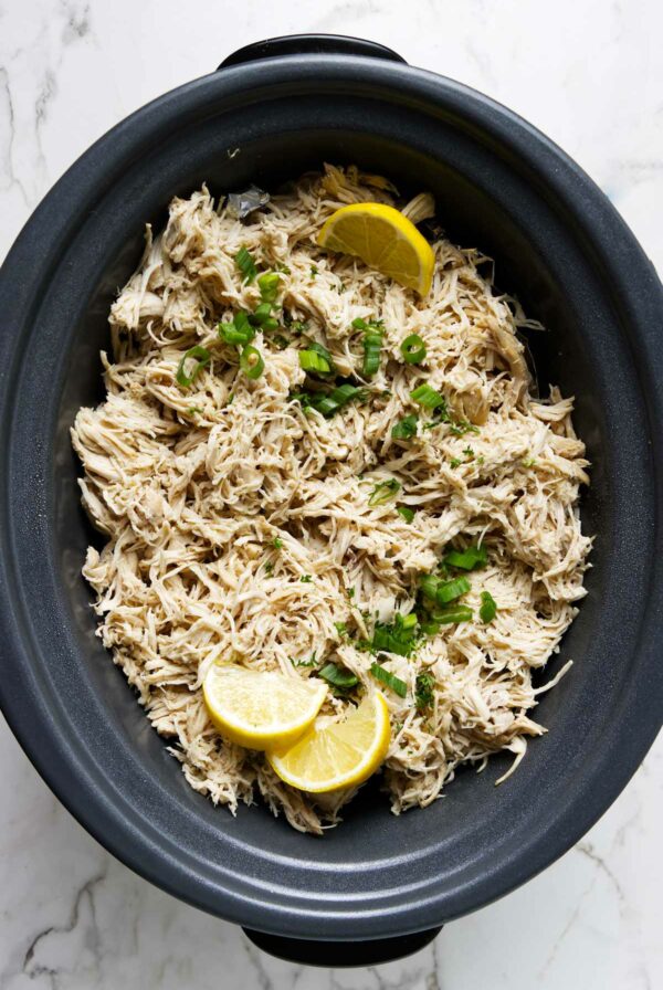 Shredded chicken with lemon and herbs in a black slow cooker.