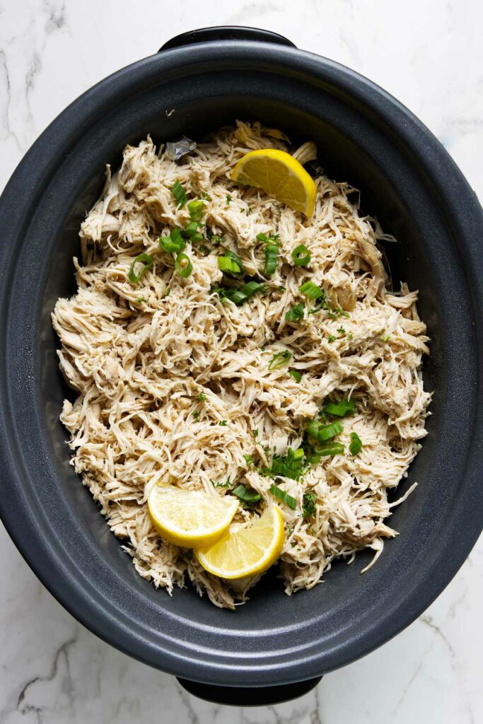 Shredded chicken with lemon and herbs in a black slow cooker.