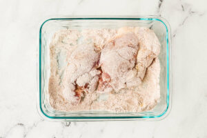 Dredging chicken thighs in flour and seasonings.