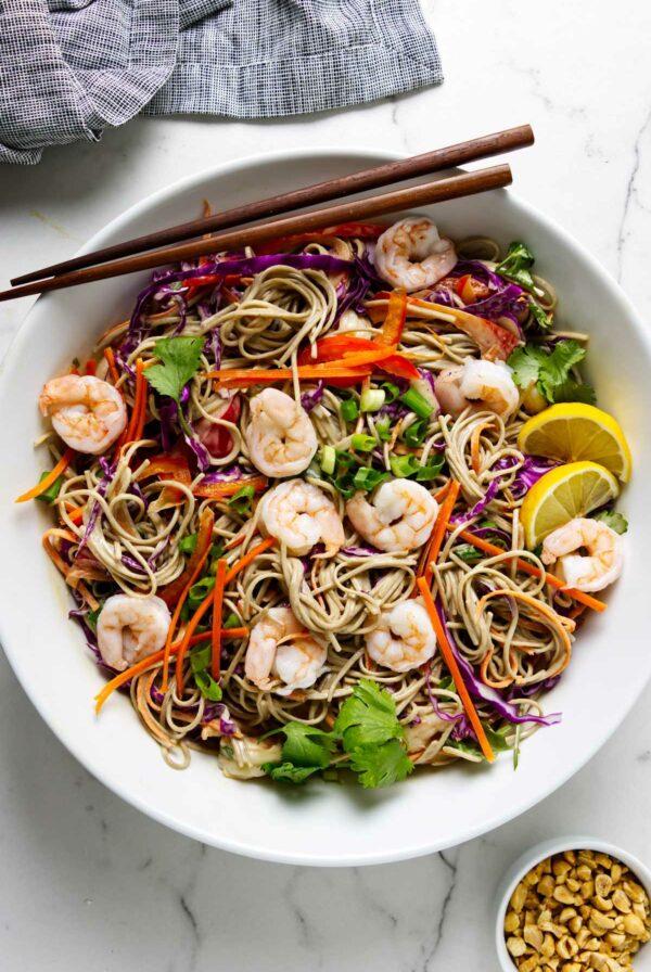 Soba noodle salad in a white bowl with chopsticks on the side.