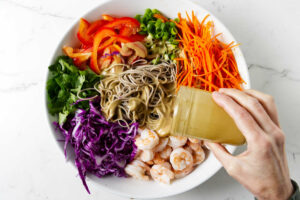 Pouring dressing over the salad with soba noodles.