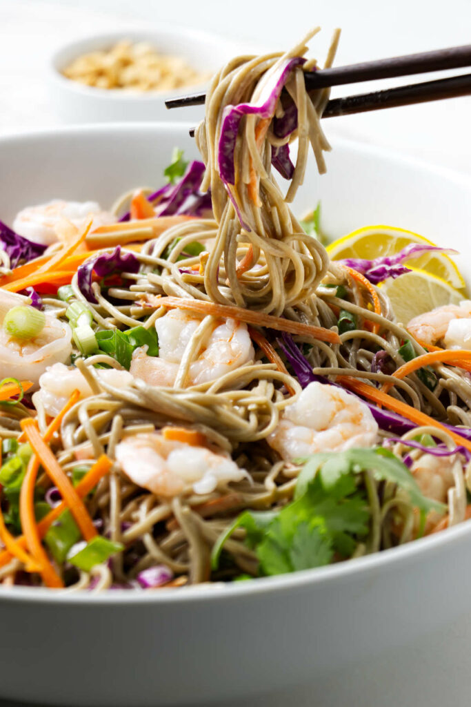 Chopsticks picking up cold soba noodles with veggies.
