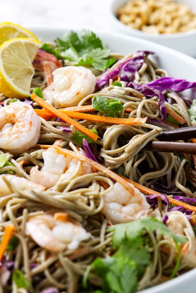 A soba noodle salad with shrimp and veggies in a white dish.