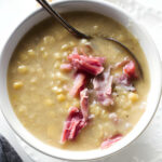 A spoon in a bowl of yellow pea soup with smoked ham.