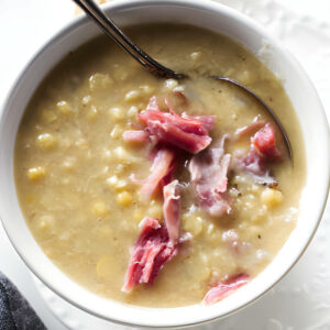 A spoon in a bowl of yellow pea soup with smoked ham.