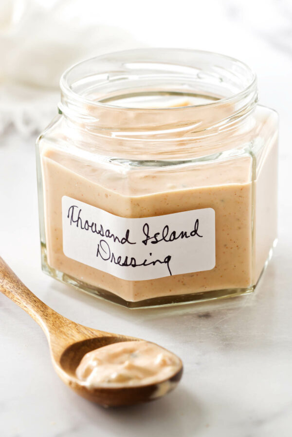 Jar of Thousand Island dressing on marble, wooden spoon with dressing in front.
