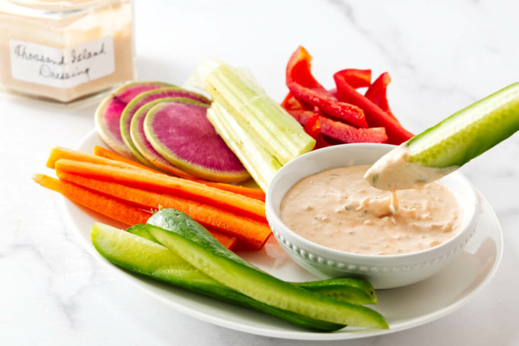 Veggies getting dipped into a dish of thousand island salad dressing.