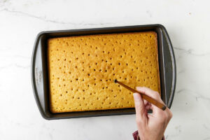 Poking holes in the cake with a skewer.
