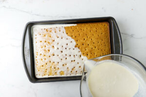 Pouring a milk mixture over a warm sponge cake.