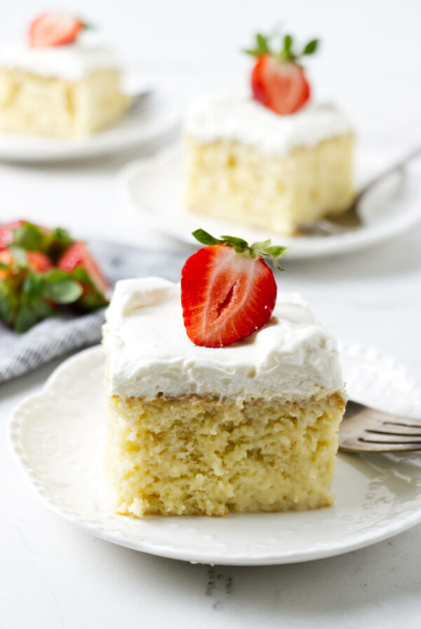 Three slices of tres leches cake on white plates topped with strawberries.