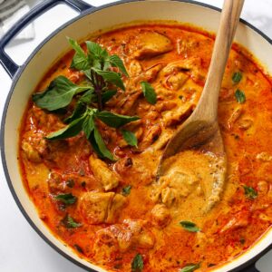 White pot of Thai panang chicken curry with basil, stirred by a wooden spoon.