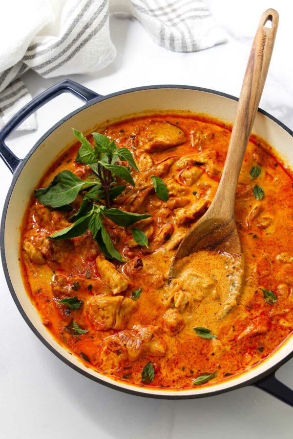 Pot of creamy panang curry with chicken and basil, stirred with a wooden spoon.