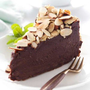 A slice of a flourless chocolate cake on a plate topped with sliced almonds.
