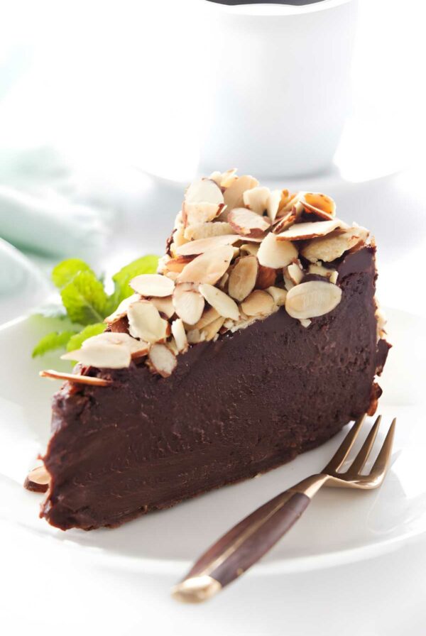 Flourless chocolate cake slice with almonds on white plate, gold fork, mint garnish.