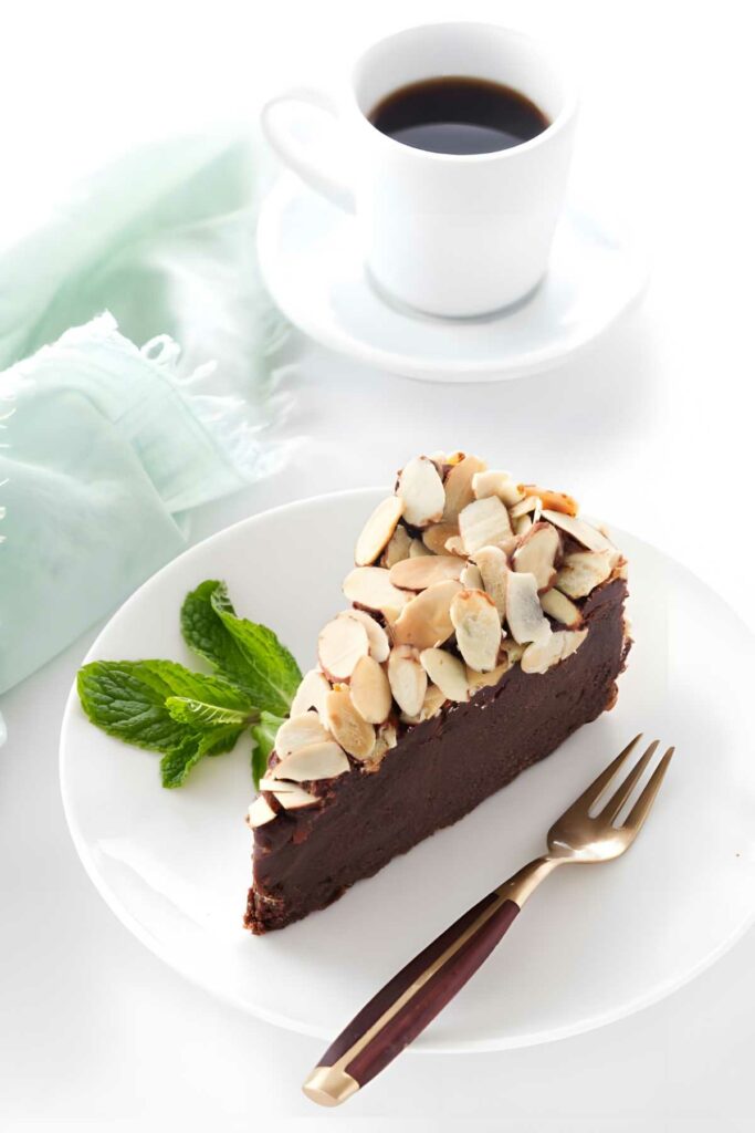 Chocolate truffle cake with almonds on a plate, beside black coffee.