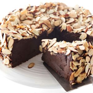 Chocolate cake with sliced almonds on stand; slice lifted to show fudgy center.
