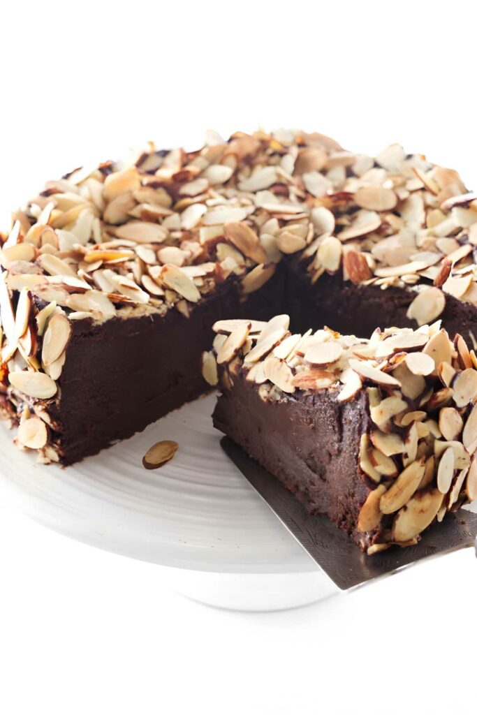Chocolate cake with sliced almonds on stand; slice lifted to show fudgy center.
