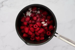 Raspberries and sugar in a saucepan.