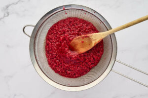Pressing the raspberry sauce through a metal strainer.